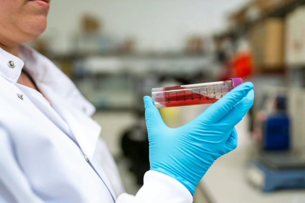 About us — A lab technician in blue gloves holds a test tube containing red liquid, showcasing measurements against a laboratory backdrop.
